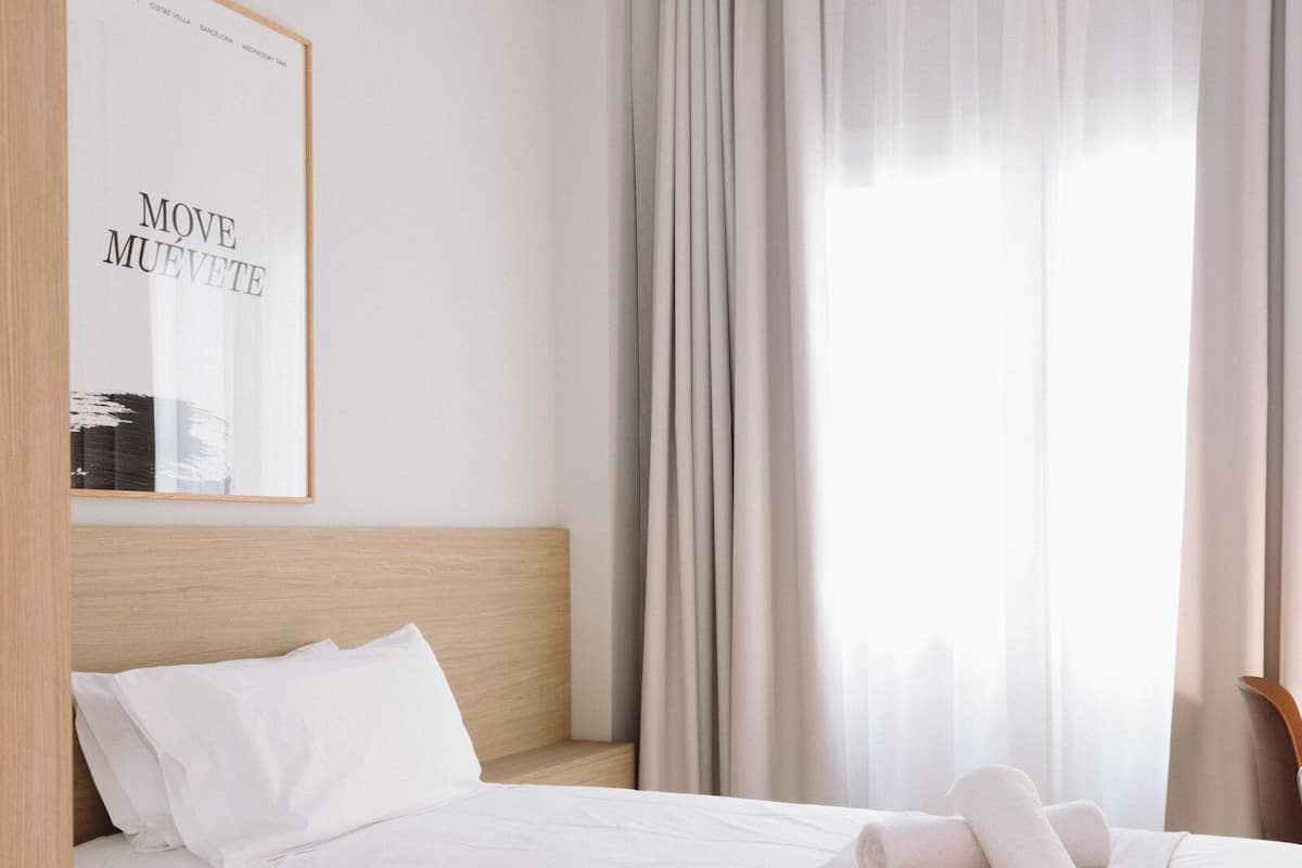 A hotel room with a bed, a framed motivational poster, a window with curtains, and a wooden headboard.