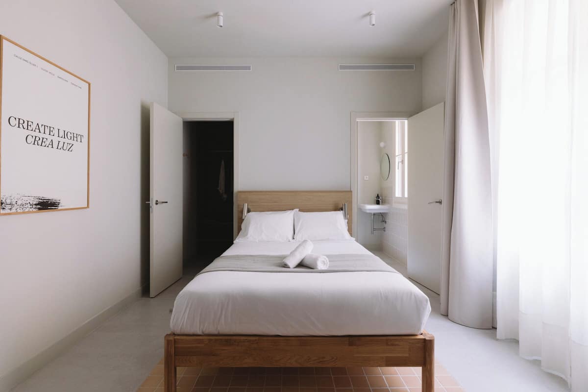 A neatly made bed with white linens and a rolled towel, a wooden headboard, and a framed artwork on the wall.