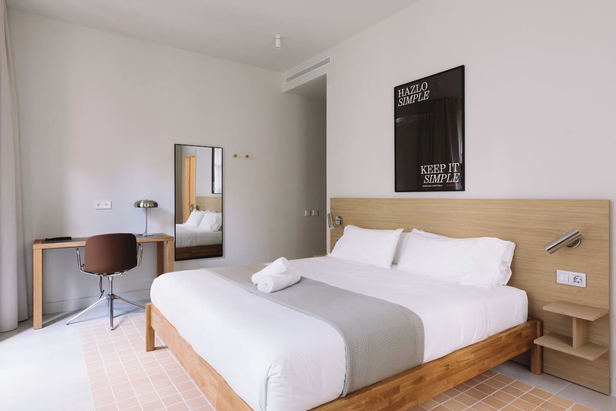 A modern hotel room with a wooden bed, a desk, and a chair.