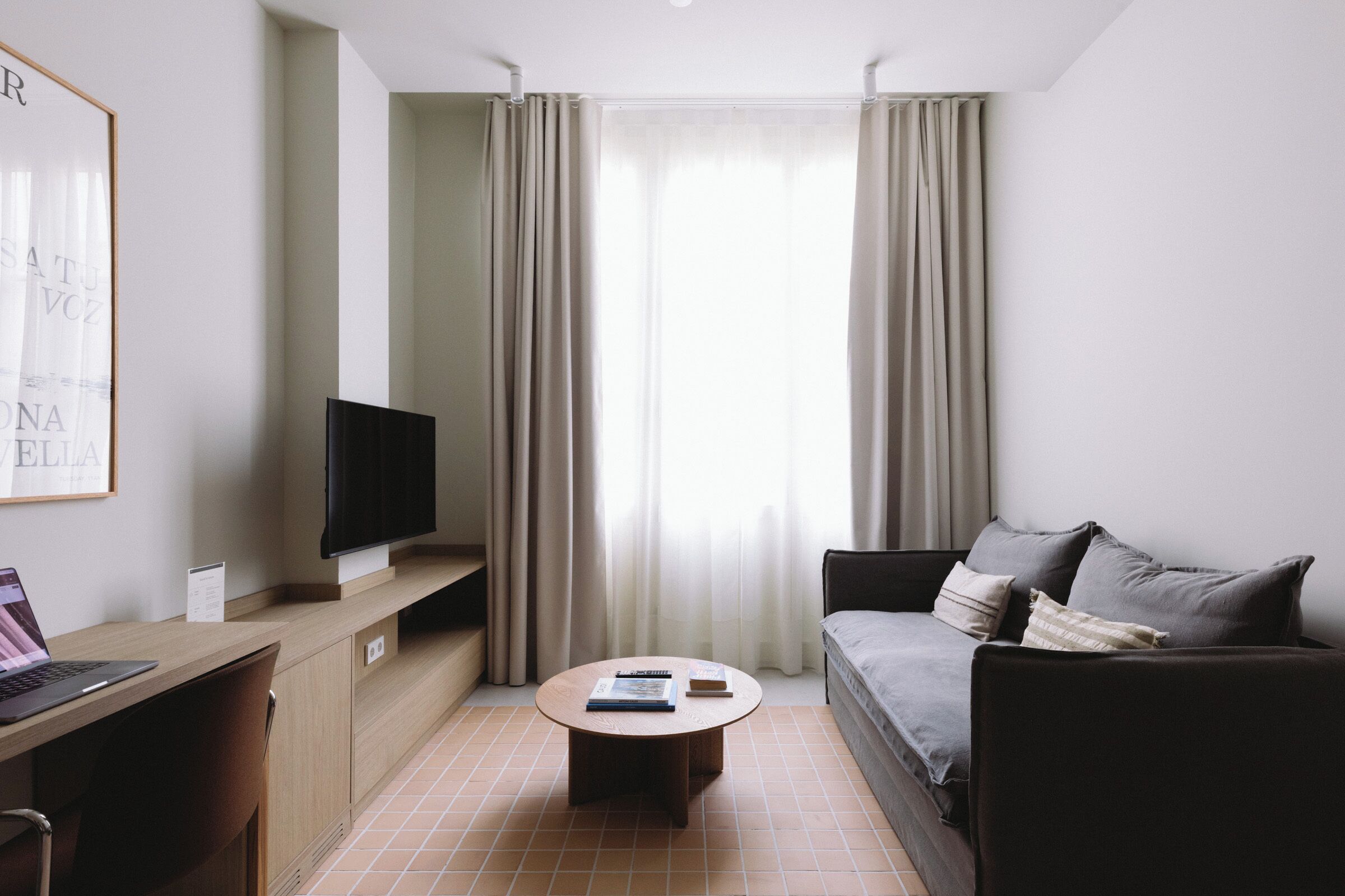 Habitación de hotel moderna con televisor de pantalla plana, una mesa de centro redonda, un sofá y un escritorio con una computadora portátil.