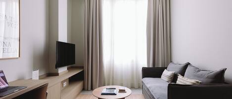 Habitación de hotel moderna con televisor de pantalla plana, una mesa de centro redonda, un sofá y un escritorio con una computadora portátil.