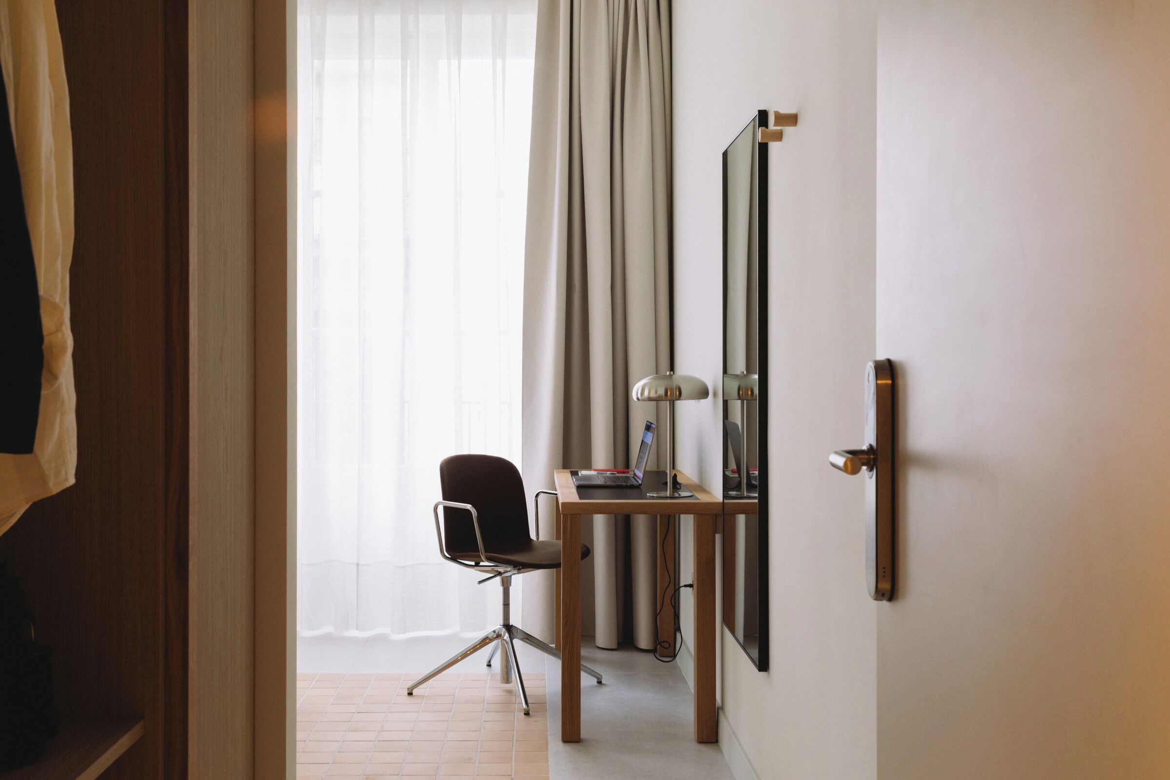 Una habitación de hotel con un escritorio de madera, una silla, una computadora portátil, una lámpara y un espejo grande en la pared.