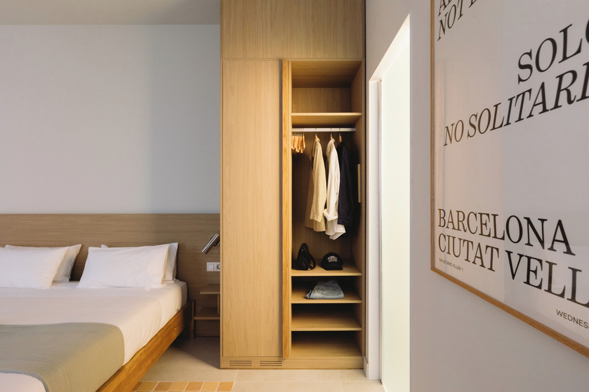 Un dormitorio con una cama de madera, un armario con ropa colgada y una pared con texto.