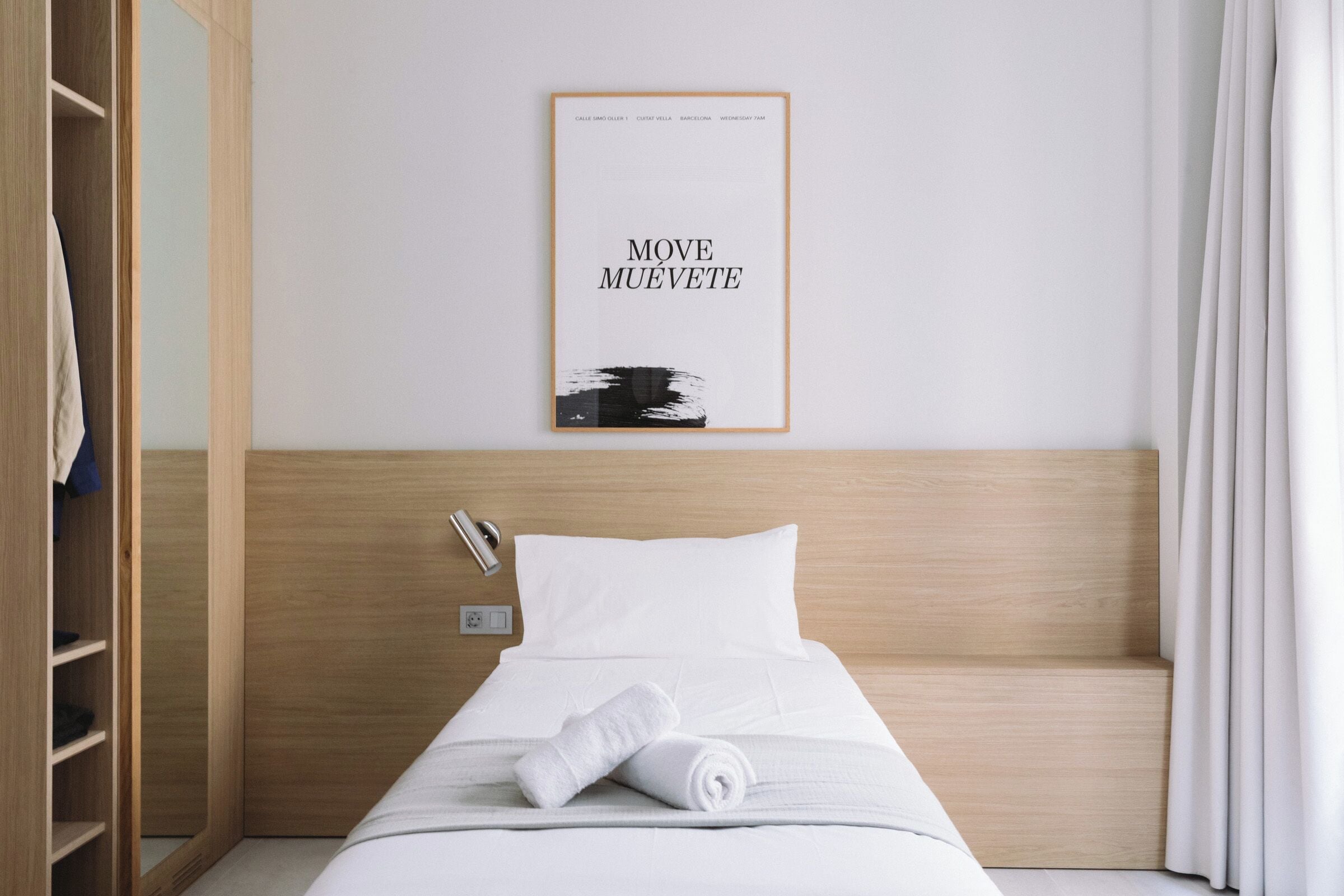 Een hotelkamer met een netjes opgemaakt bed, een houten hoofdbord, een ingelijst kunstwerk aan de muur en een garderobe.