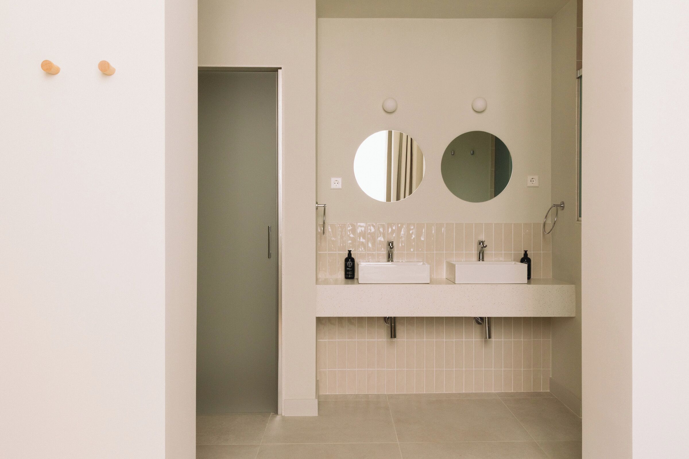 Une salle de bain moderne avec deux lavabos, un miroir et une porte donnant sur une autre pièce.
