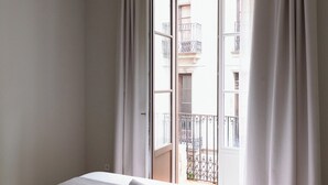 A bedroom with a bed, a window with curtains, and a view of a building outside. - Outsite Barcelona - Work, Connect, Explore (Barcelona)