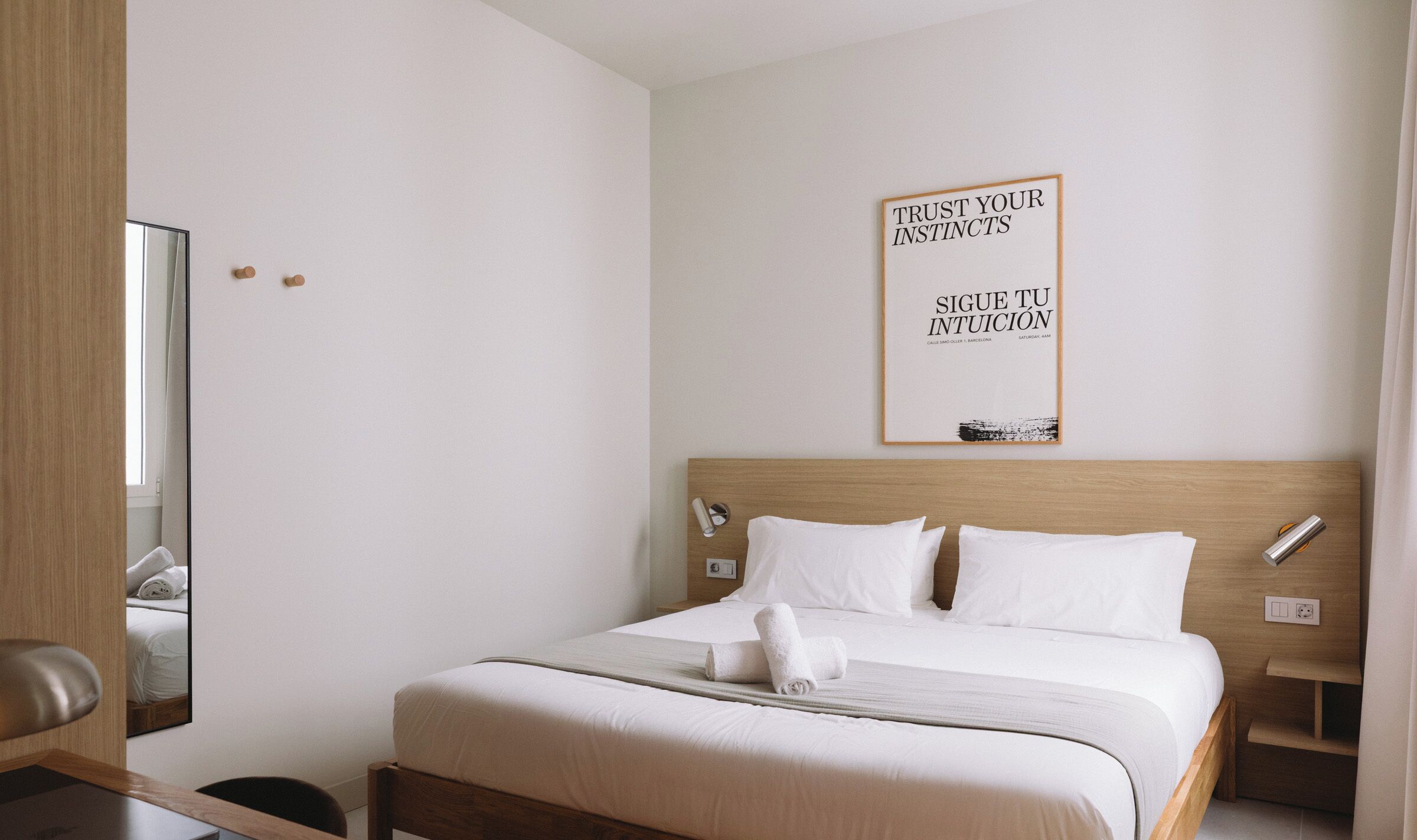 Ein Hotelzimmer mit einem großen Bett, einem Holz-Kopfstück, einem Nachttisch, einem Spiegel und einem motivierenden Zitat an der Wand.