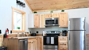 A modern kitchen with wooden cabinets, stainless steel appliances, a ceiling fan, and a window with a view. - 5 Entire Cabins Retreat (Paris)
