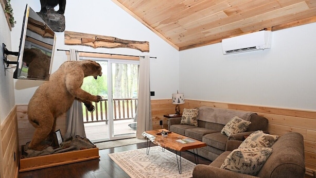 A cozy living room with a wooden ceiling, a sofa, a coffee table, and a bear statue. - 5 Entire Cabins Retreat (Paris)