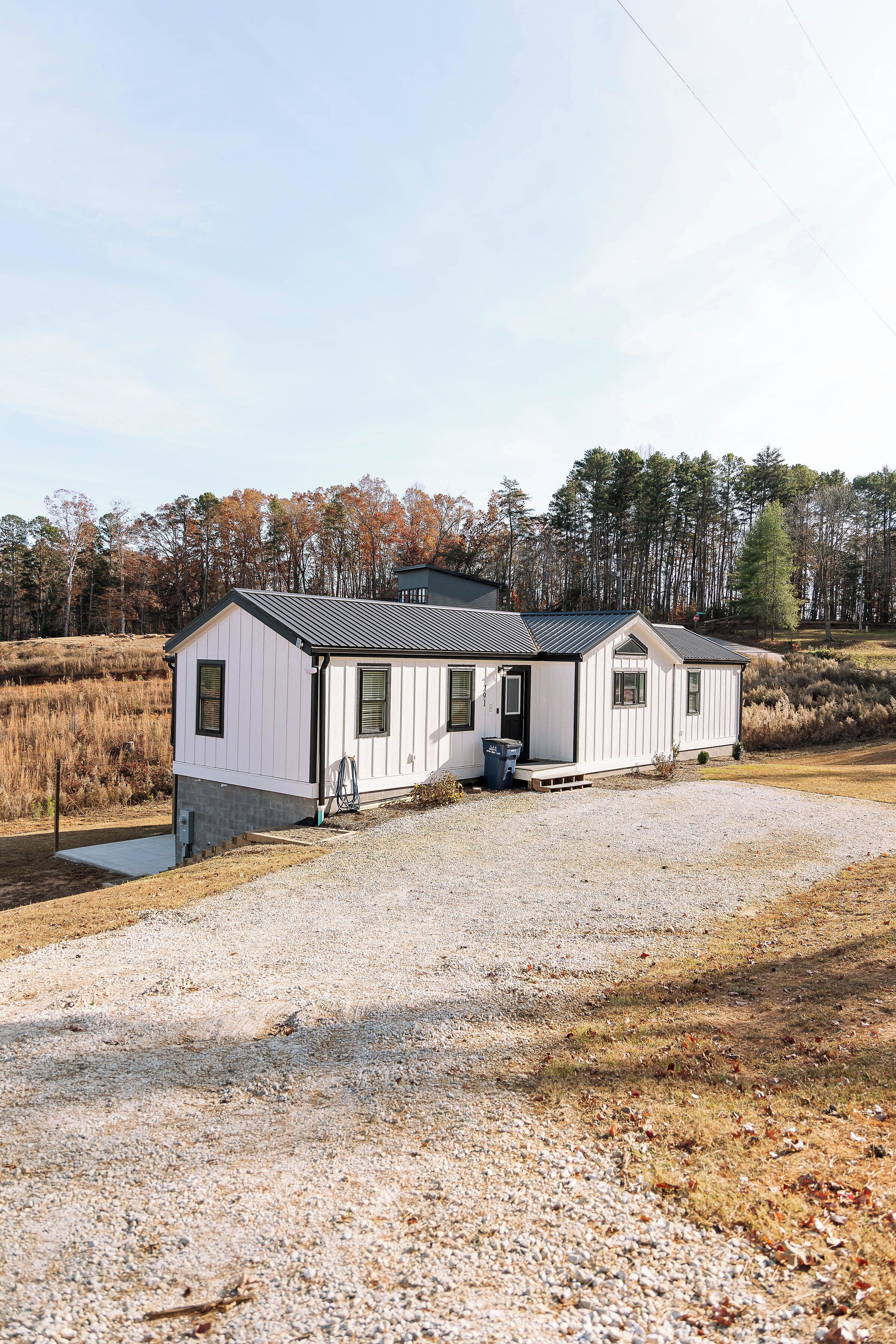 A small, single-story house with a gravel driveway and a metal roof.