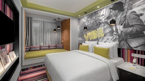 Une chambre d’hôtel moderne dotée d’un grand lit, d’un coin salon avec des coussins, d’une télévision et d’une fresque murale.