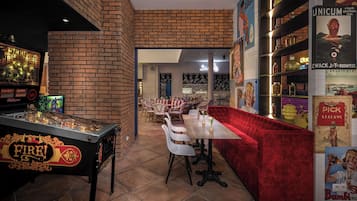Una mesa de billar con temática 'Fire!', un sofá de terciopelo rojo y una zona de bar con estanterías y botellas.