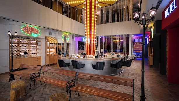 Un hall d’hôtel doté d’un bar central, de bancs en bois et d’un lustre.