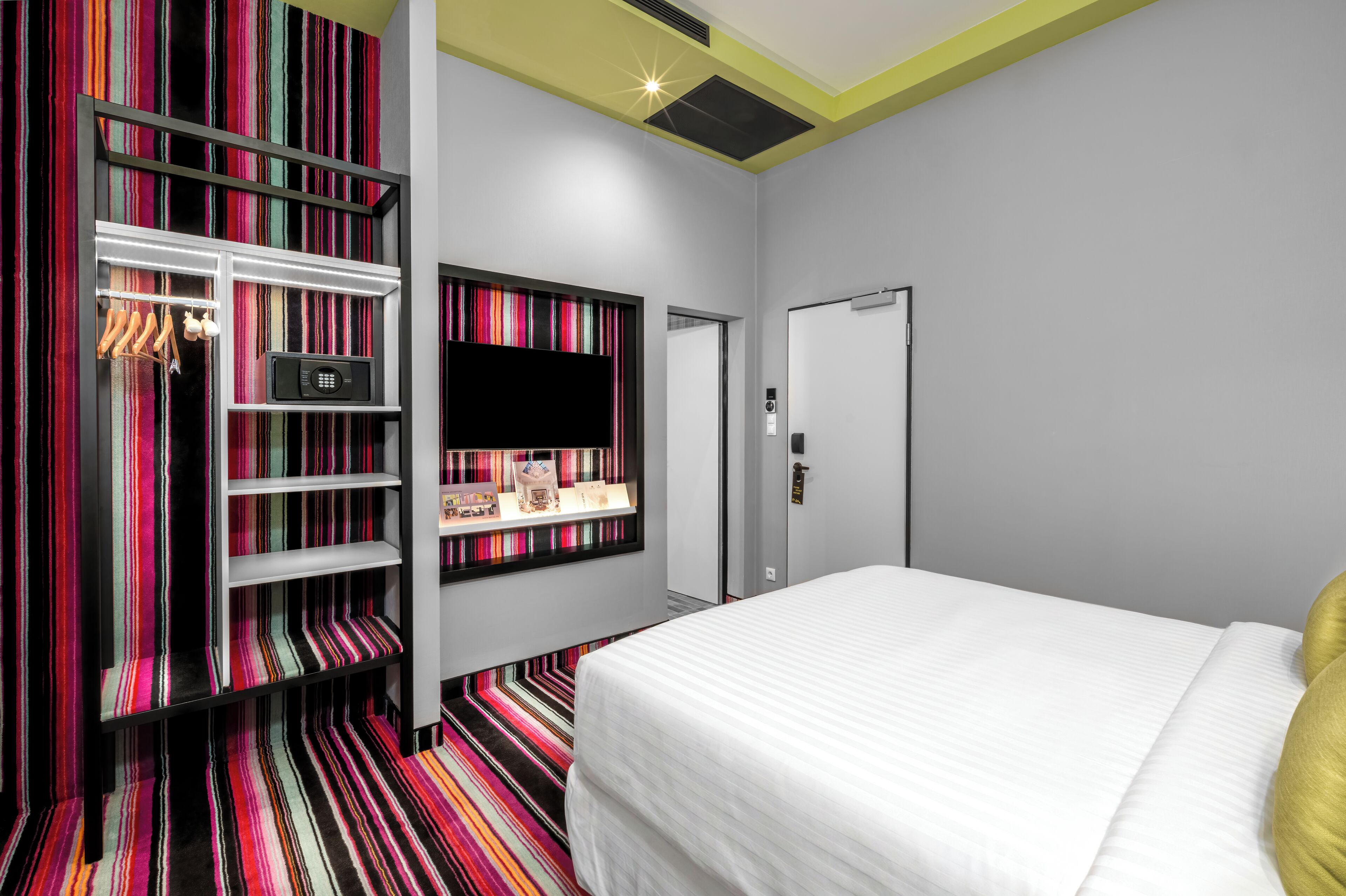 A hotel room with a bed, a wardrobe, a television, and a shelf with items.