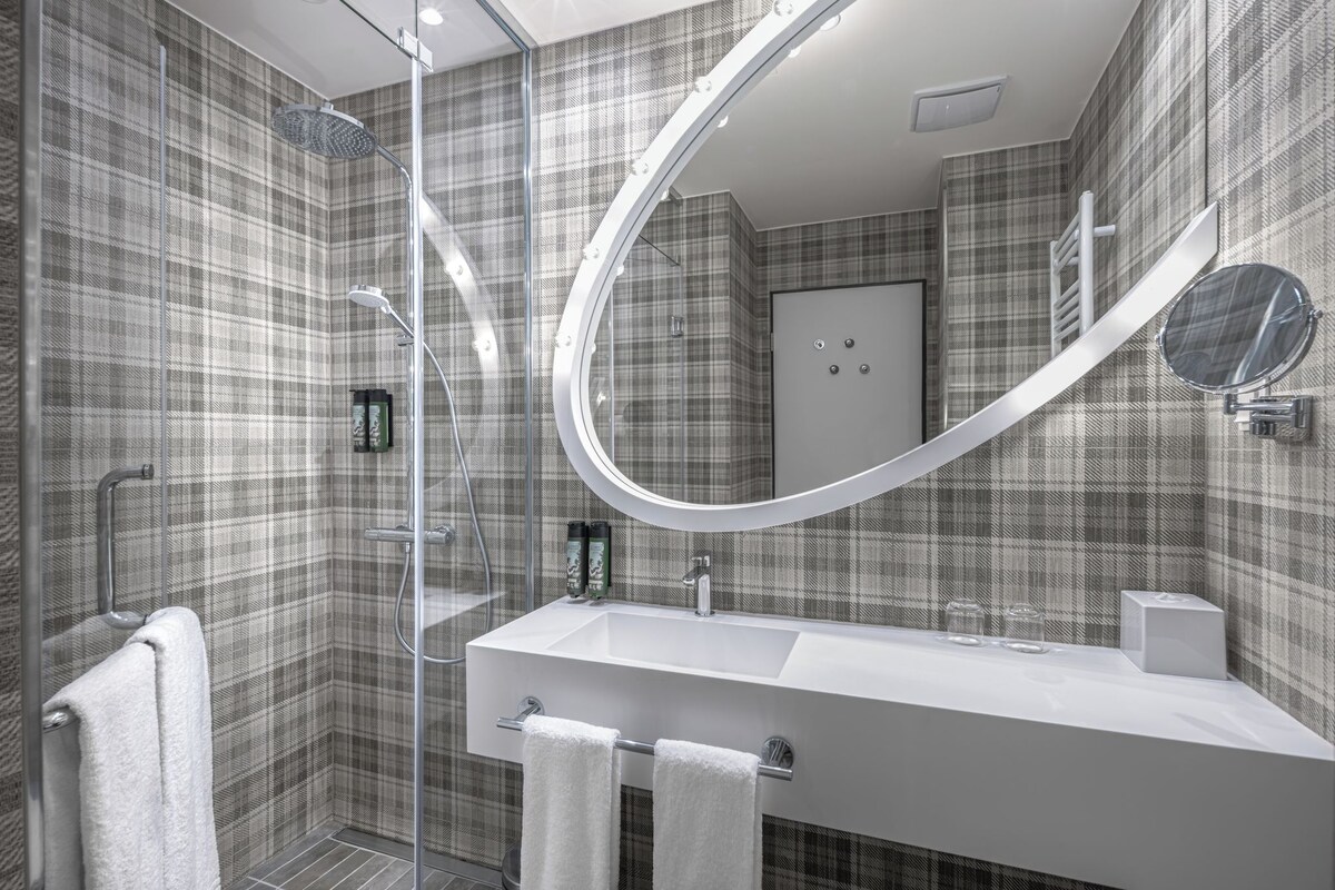Un bagno moderno con doccia, uno specchio grande e un lavandino bianco.