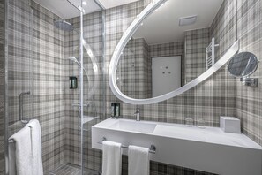 Une salle de bain moderne avec un grand miroir, une douche et un lavabo blanc.