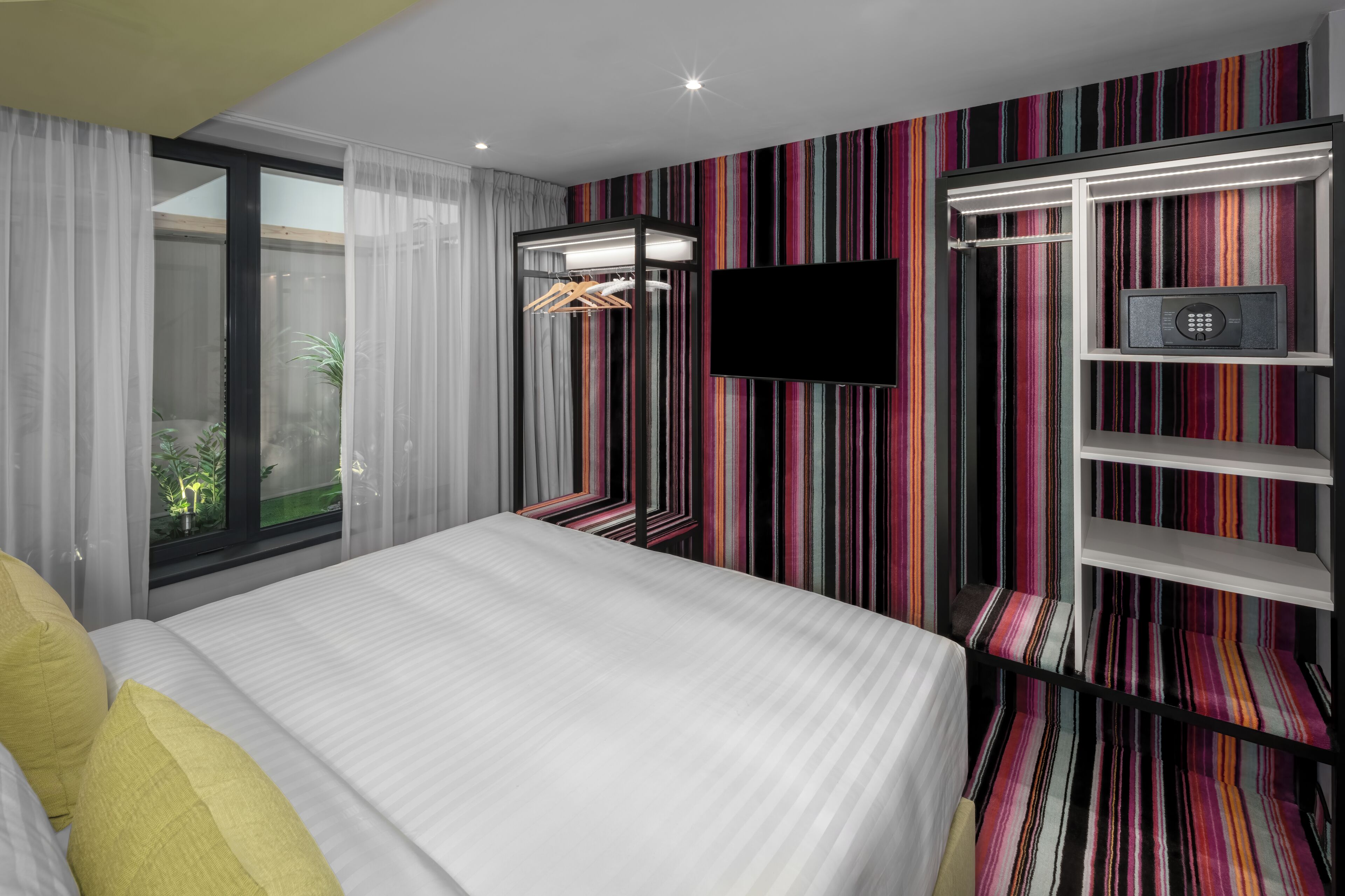 Habitación de hotel con cama, televisión, armario y pared a rayas.