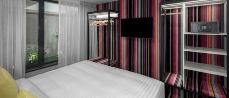 A hotel room with a bed, a TV, a wardrobe, and a striped wall.