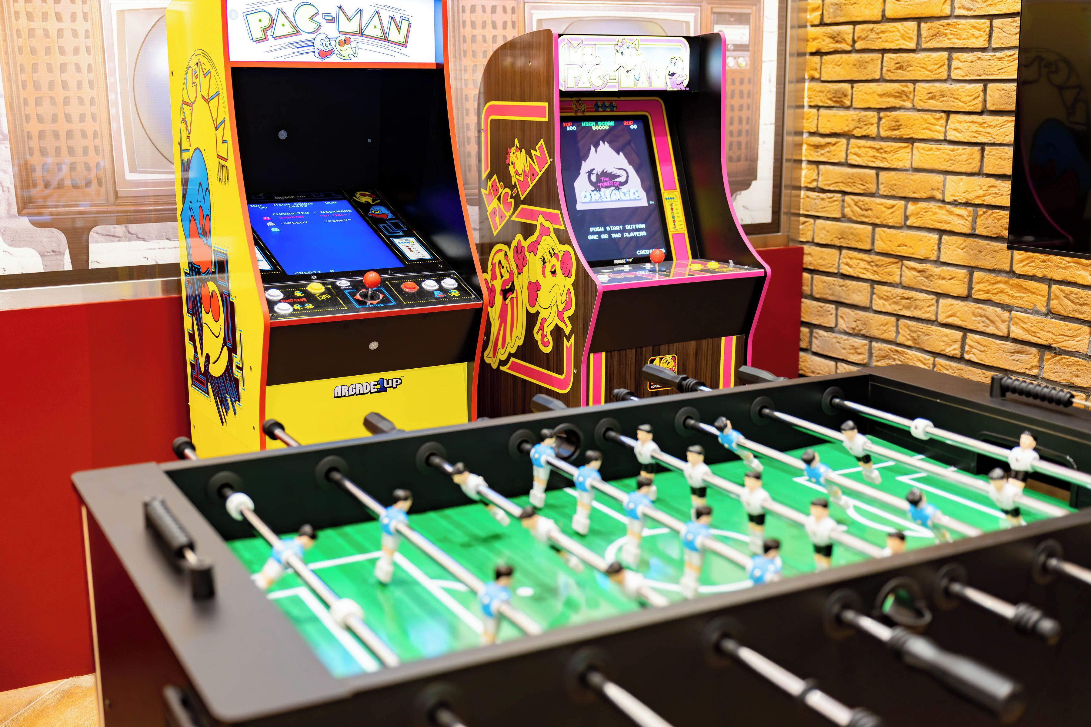 Two arcade foosball tables with a brick wall and a window in the background.
