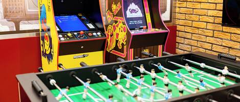 Deux tables de baby-foot d’arcade, avec un mur de briques et une fenêtre en arrière-plan.