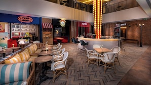 Un espace intérieur moderne doté d’un bar central, de différents espaces de détente et de vitrines donnant sur des boutiques, notamment un hôtel et un magasin appelé « DMS ».