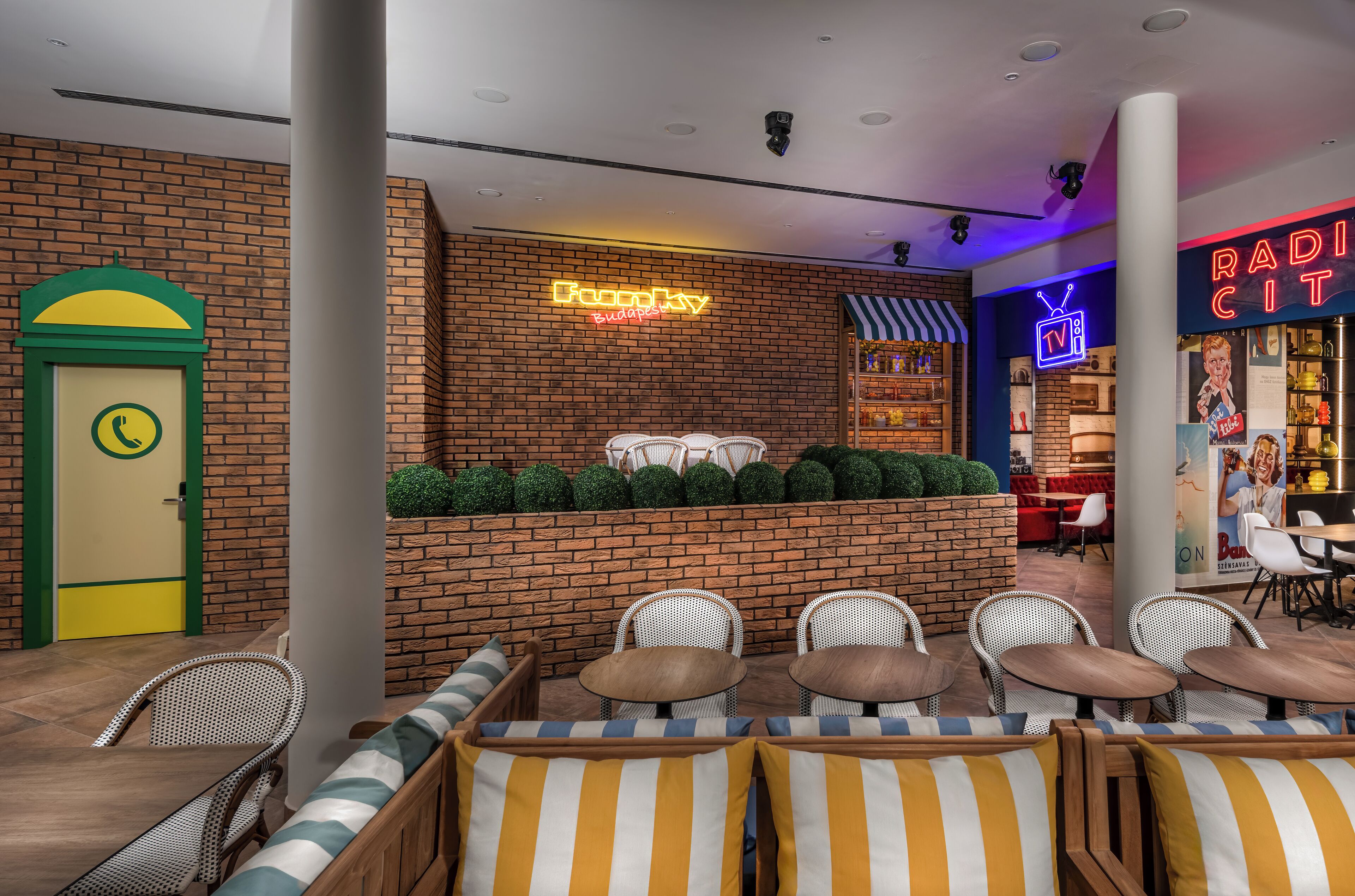 Un restaurant aux murs de briques, aux enseignes lumineuses et doté d’une terrasse avec des coussins à rayures.