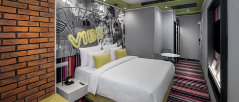 Una habitación de hotel moderna con una pared de ladrillo decorativa, una cama grande con ropa blanca, una alfombra colorida a rayas y un televisor montado en la pared.