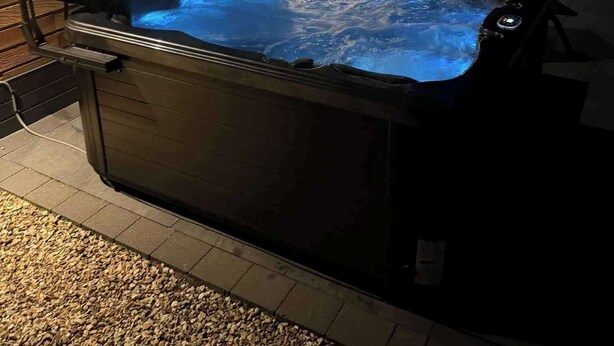 Ein Whirlpool mit erhöhtem Rand und Bedienfeld, draußen gelegen, mit einer sichtbaren Terrassenfläche im Hintergrund.