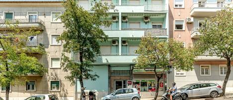 Un edificio de varios pisos con balcones, un coche estacionado y una motocicleta.