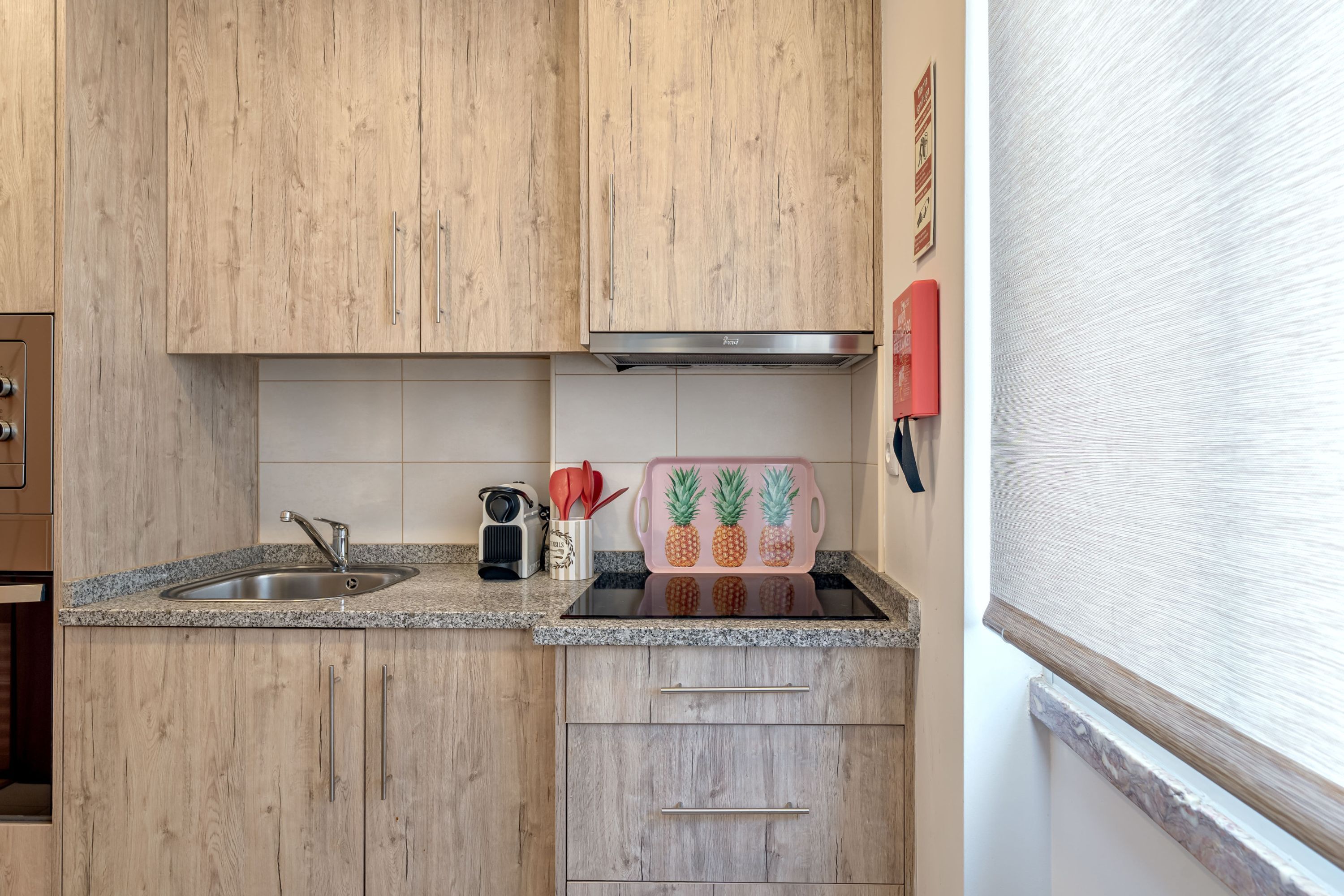 Une cuisine avec des meubles en bois, un plan de travail en granit, un évier en acier inoxydable et un appareil de cuisine rouge.