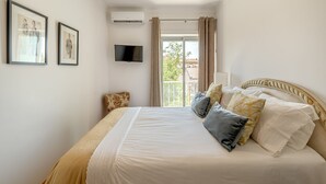 Un dormitorio ordenado con una cama grande, un televisor de pantalla plana y un ventanal con cortinas.