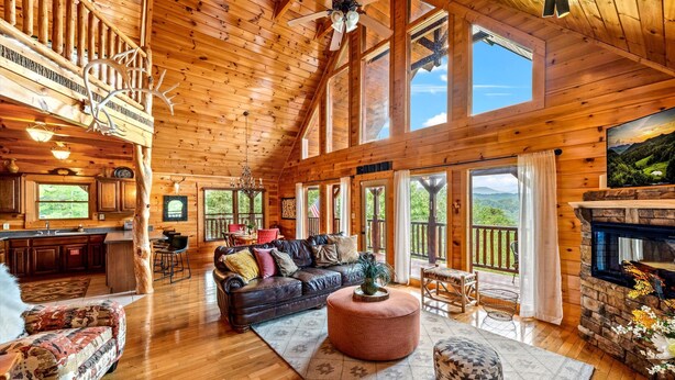 A spacious cabin with a high ceiling, wooden walls, a fireplace, a large sofa, and a dining area. - Mountain Views • Hot Tub • Minutes to Dollywood (Sevierville)