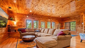 A spacious living room with wooden walls and ceiling, a large sectional sofa, a coffee table, and a rug. - Mountain Views • Hot Tub • Minutes to Dollywood (Sevierville)