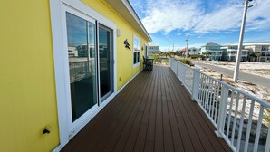 Un edificio amarillo con terraza de madera y barandillas blancas.