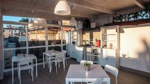 A modern kitchen with white cabinets, a dining area with white chairs, and large windows offering views of the city. - Solarium al Duomo Rooms by Wonderful Italy (Naples)