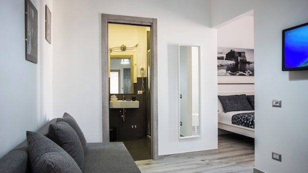 A modern hotel room with a grey sofa, a bed with patterned bedding, a large mirror, and a television on the wall. - Solarium al Duomo Rooms by Wonderful Italy (Naples)