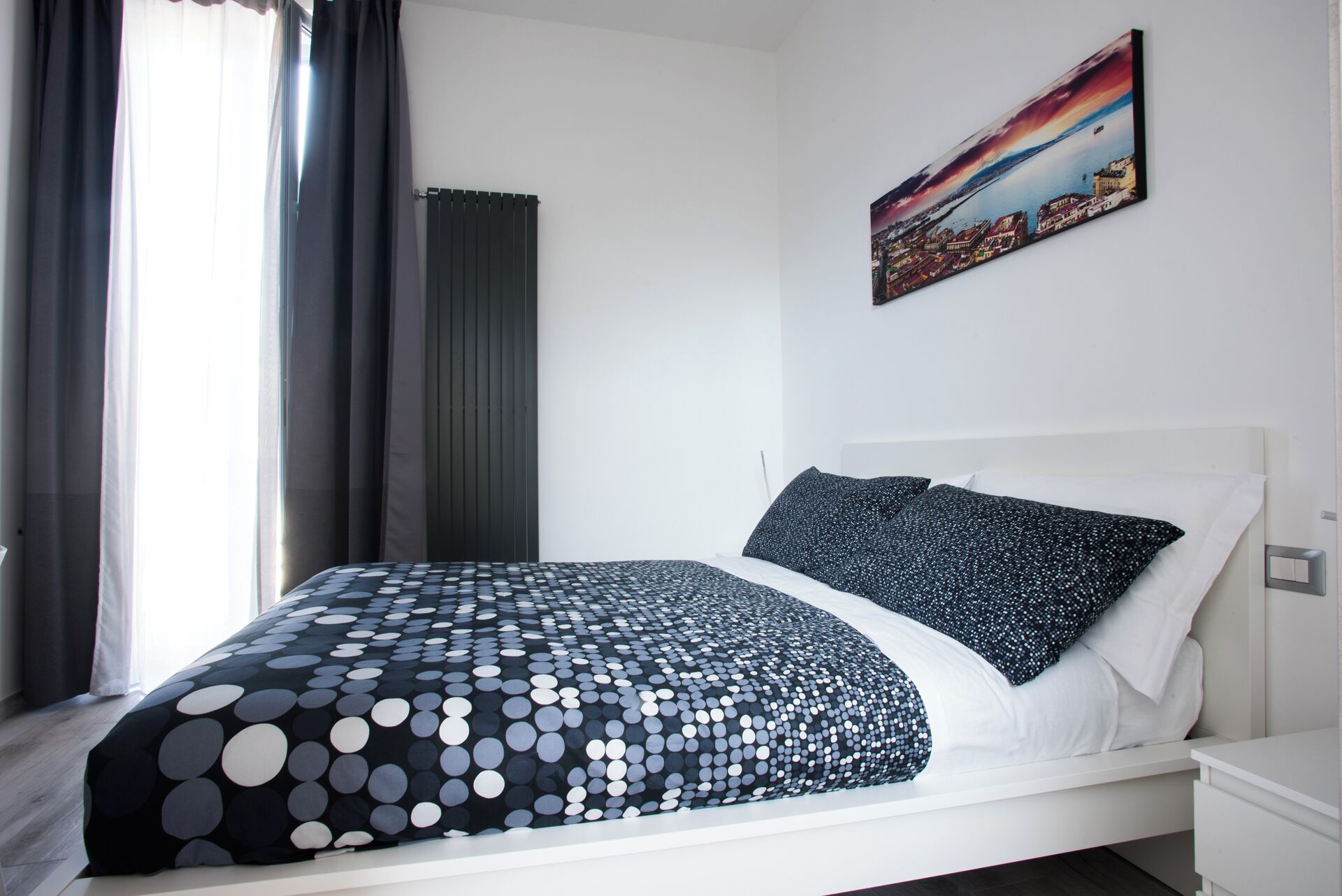A modern bedroom with a bed, a nightstand, a painting, and a window with curtains.