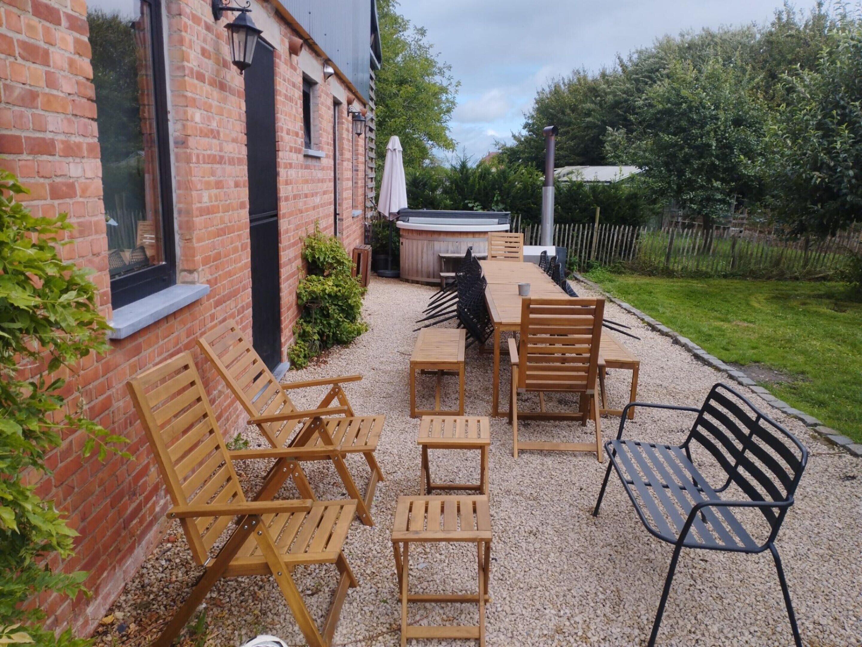A patio with wooden furniture, a hot tub, and a brick building.