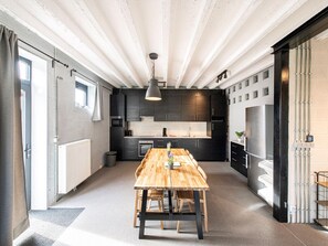 A modern kitchen with dark cabinets, a wooden dining table, and a pendant light. - Holiday Home With Garden and Roofed Terrace (Heers)