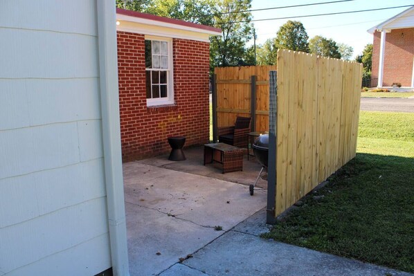 A backyard with a patio area, a wooden fence, and a brick building.