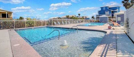 A swimming pool with clear water, surrounded by a white fence and lounge chairs.