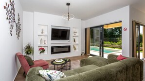 A modern living room with a flat-screen TV, a fireplace, and a glass door leading to a pool. - Vila SUNLIFE with pool&sauna by Villas Guide (Matulji)