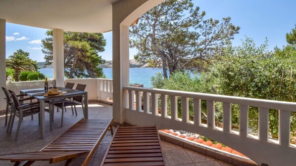 Un espace extérieur abrité, avec une table et des chaises, un banc en bois, et une vue sur la mer et les arbres.
