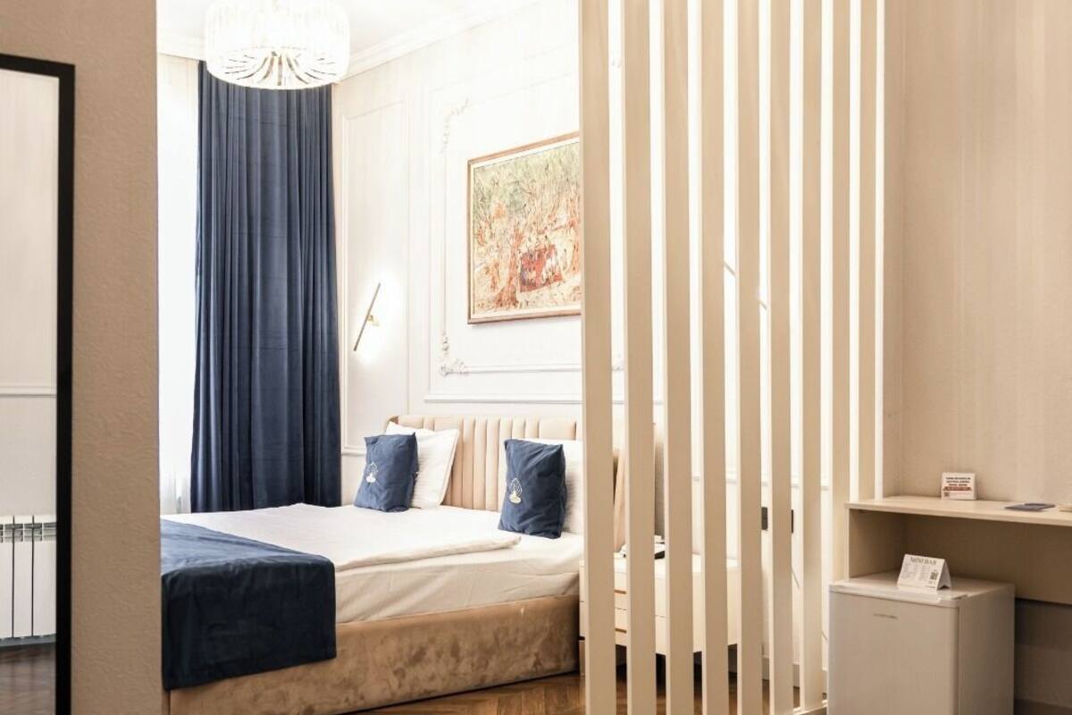 A modern bedroom with a bed, a nightstand, a small refrigerator, and a sliding door.