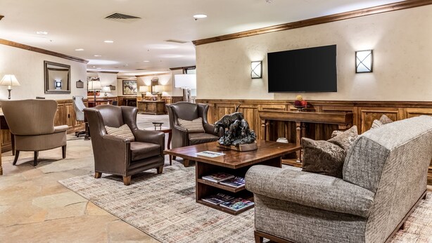 Uma sala de estar espaçosa com poltronas de couro, uma mesa de centro com revistas, uma TV de tela plana na parede e uma parede de destaque em madeira.