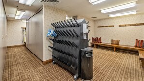 Quarto de hotel com um eletrodoméstico preto grande, possivelmente uma máquina de café, um banco com almofadas e uma lixeira.