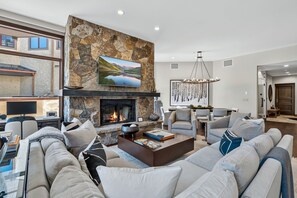 A modern living room with a stone fireplace, comfortable seating, and a large flat-screen TV. - Contemporary Condo by InvitedHome | Ski-In/Out, Base of Village, Balcony, Views (Avon)