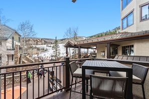 A balcony with a table and chairs, overlooking a ski slope with people skiing.