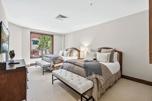 A bedroom with a bed, bedside table, lamp, bench, and a view of the outdoors through a window. - Contemporary Condo by InvitedHome | Ski-In/Out, Base of Village, Balcony, Views (Avon)