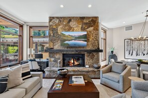 Una sala de estar moderna con chimenea de piedra, un televisor de pantalla plana y vistas a un paisaje montañoso.